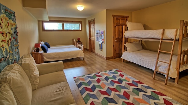 Une pièce chaleureuse avec un lit superposé, un lit simple, un bureau en bois et un tapis coloré.