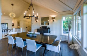 Un vaste espace dédié à la salle à manger, avec une grande table en bois, des chaises blanches et un lustre.