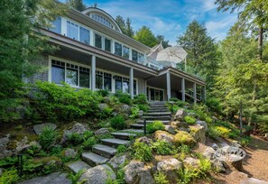 Une maison moderne dotée d’un porche abrité, d’un escalier en pierre et d’une végétation luxuriante.