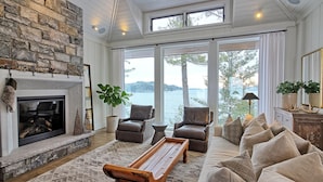 A cozy living room with a fireplace, comfortable seating, and a view of a lake. - Ultimate Boathouse Entertaining, New 6 bdrm, 8 bath Cottage/Boathouse! Hot tub! (Port Carling)