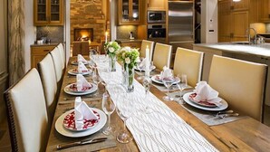 Een eetkamer met een lange houten tafel gedekt voor een maaltijd, met aan weerszijden houten kasten en een stenen open haard.