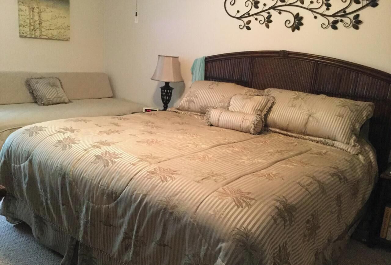 A bedroom with a large bed, a nightstand, a lamp, and a wall decoration.