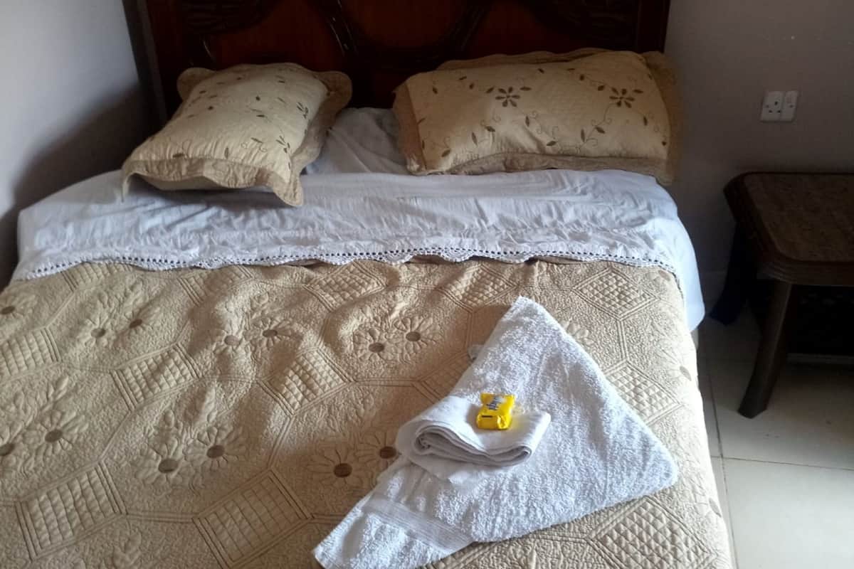 Un lit bien fait, avec une couvre-lit matelassé, deux oreillers et une serviette pliée sur laquelle repose un objet jaune.