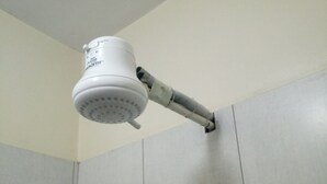A bathroom with a white shower head mounted on a wall, a towel rack, and tiled walls. - 2030 Guest House (Nakuru)