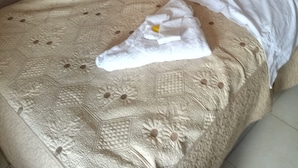 A neatly made bed with a patterned bedspread, pillows, and a folded towel. - 2030 Guest House (Nakuru)