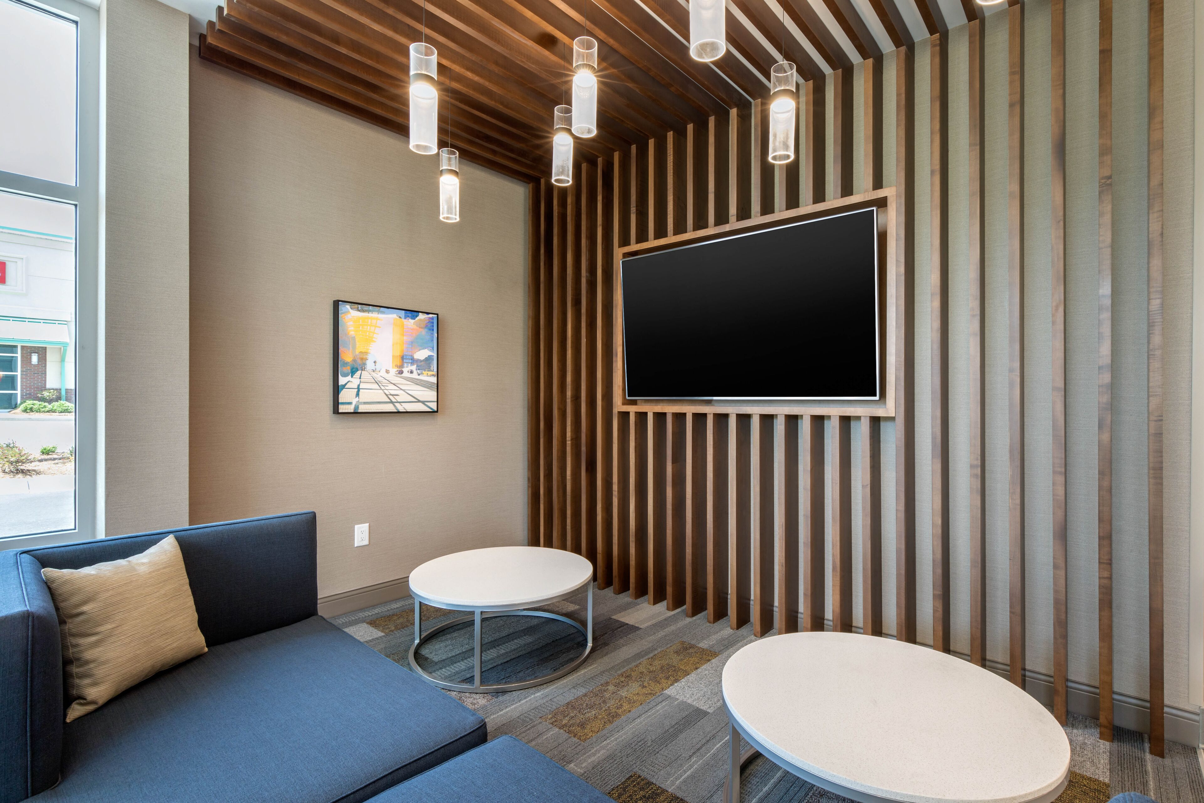 A modern waiting area with a sofa, two round tables, a mounted TV, and vertical wooden slats on the wall.