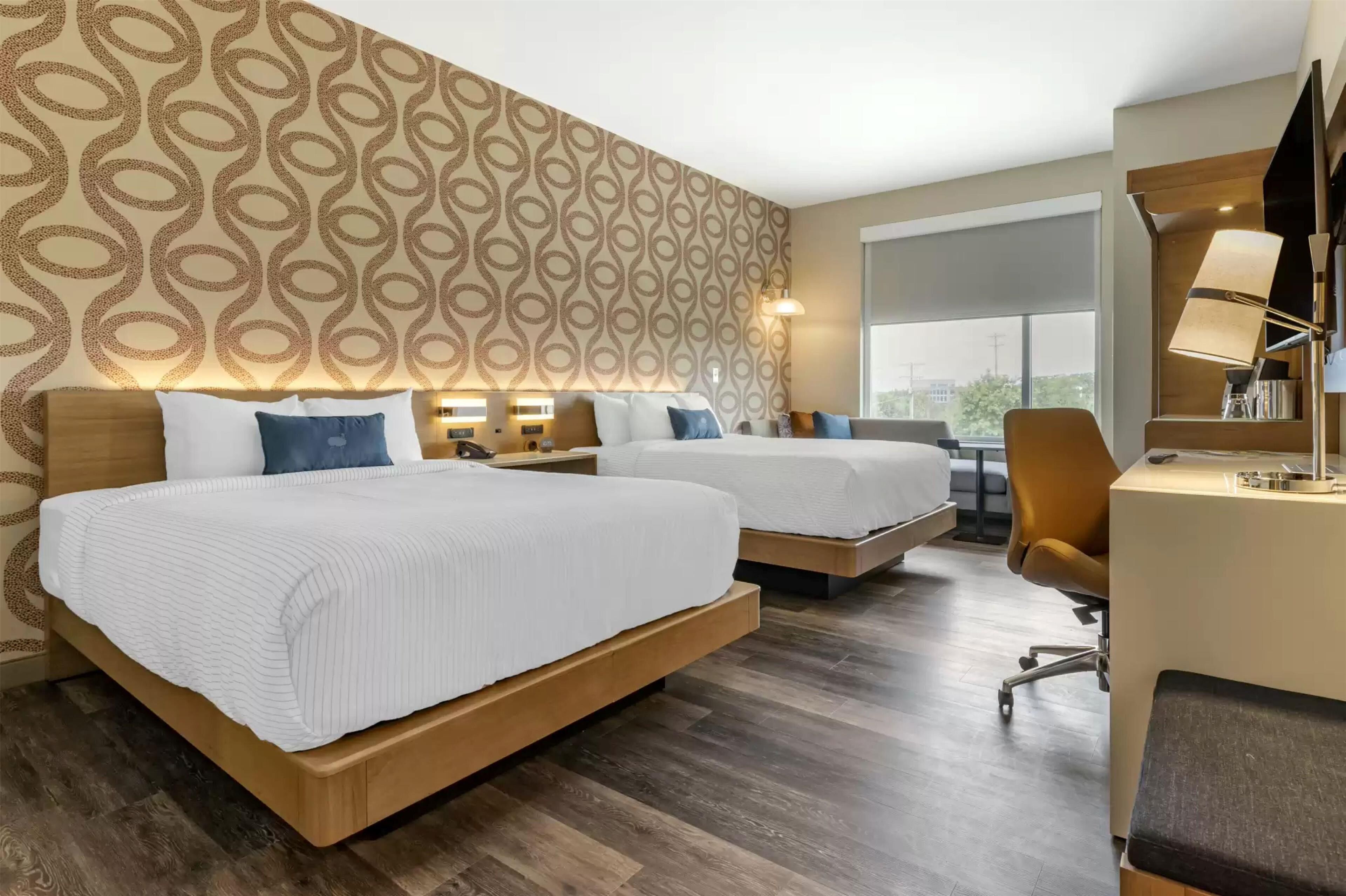 Una habitación de hotel con dos camas, un escritorio y un ventanal grande.