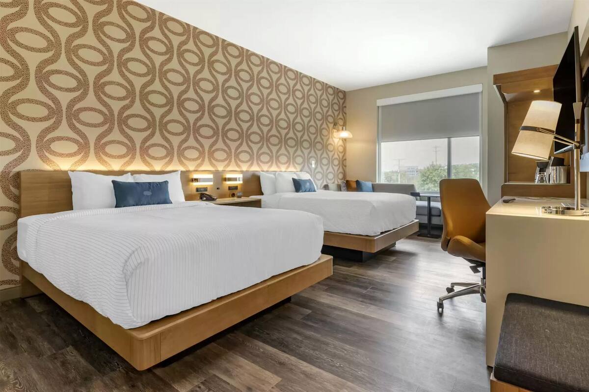 Ein Hotelzimmer mit zwei Betten, einem Schreibtisch und einem großen Fenster.