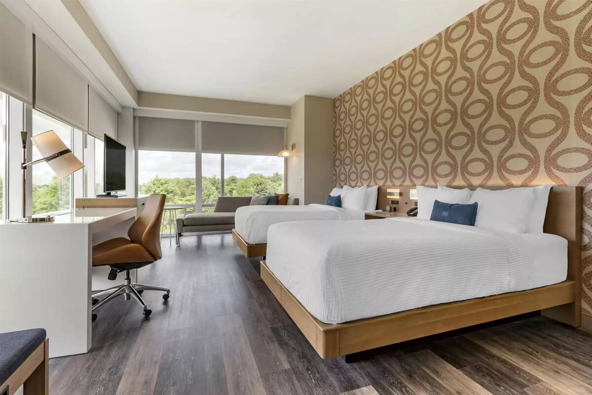Ein Hotelzimmer mit zwei Betten, einem Schreibtisch, einem Stuhl und einem Fernseher.
