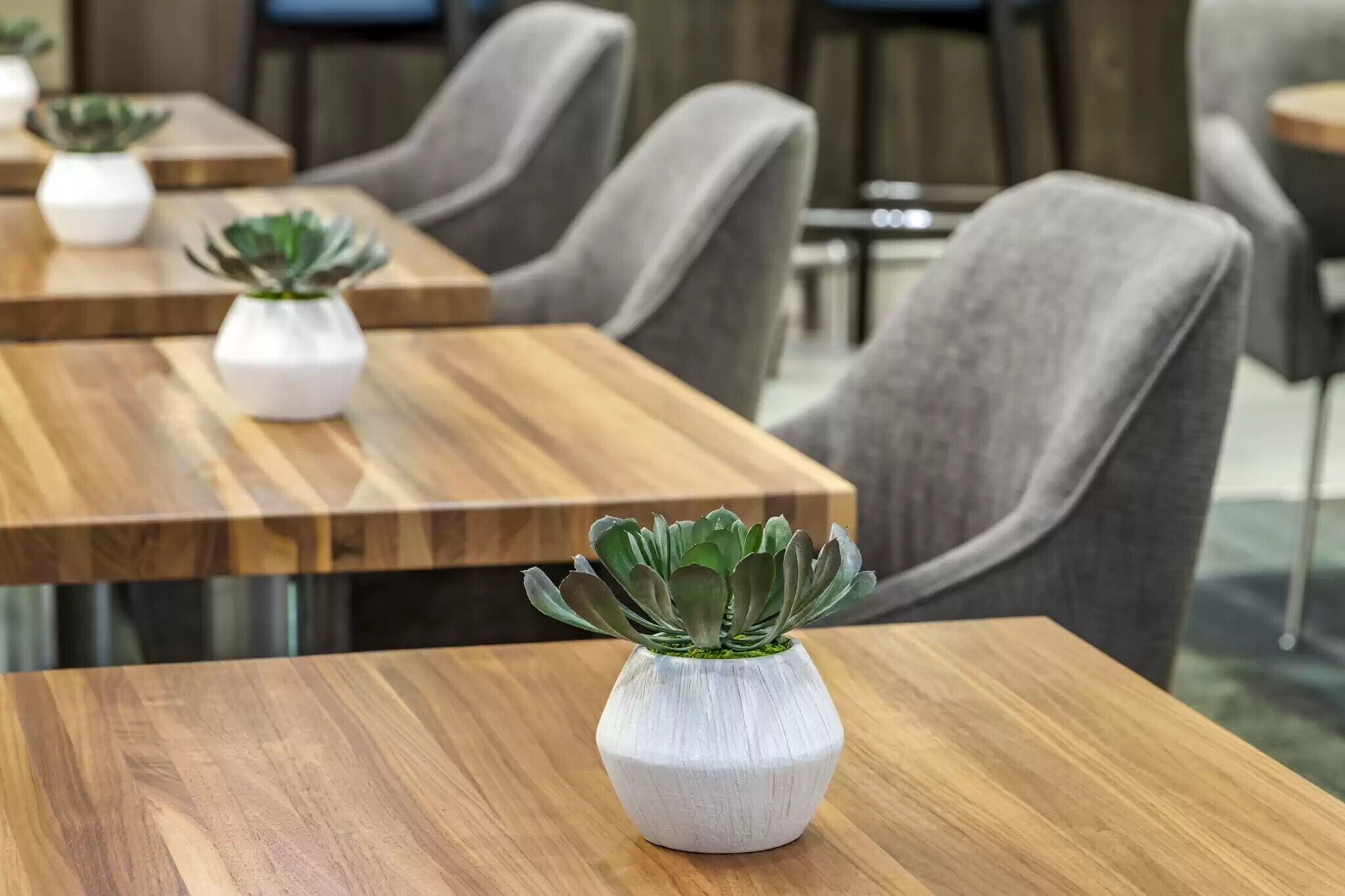 A modern dining area with wooden tables and grey upholstered chairs.