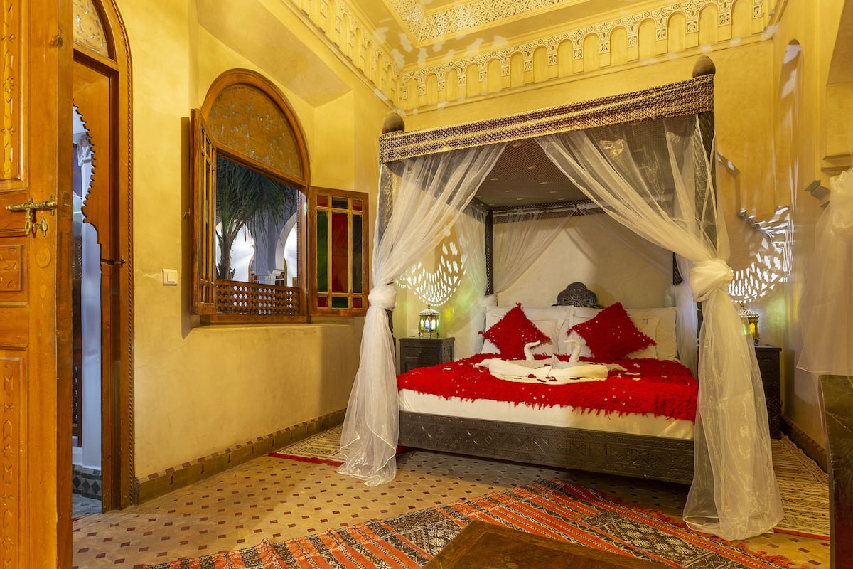 A four-poster canopy bed with a red bedspread, a mirror, and a patterned rug.
