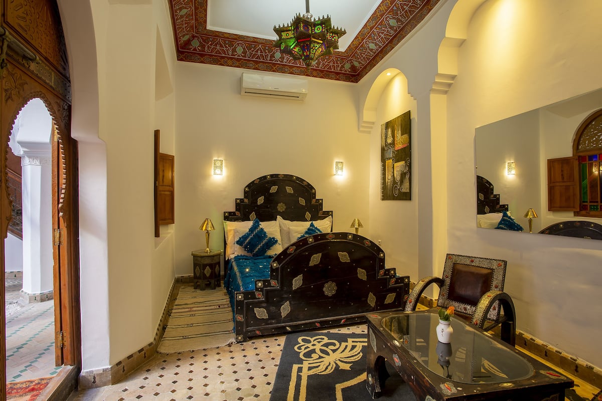 A traditional room with a bed, a glass coffee table, and a chair.
