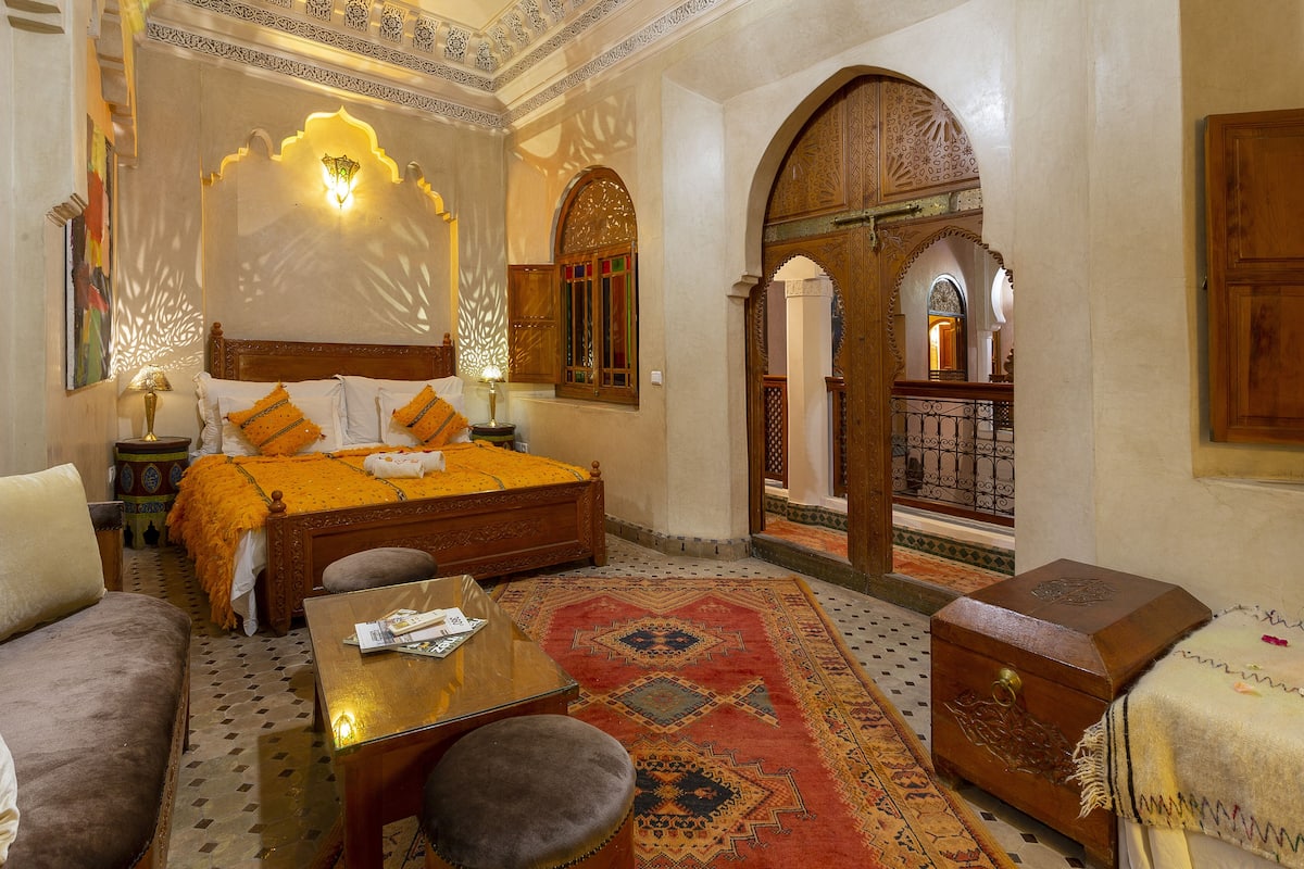 A traditional room with a bed, a sofa, a table, and a decorative rug.