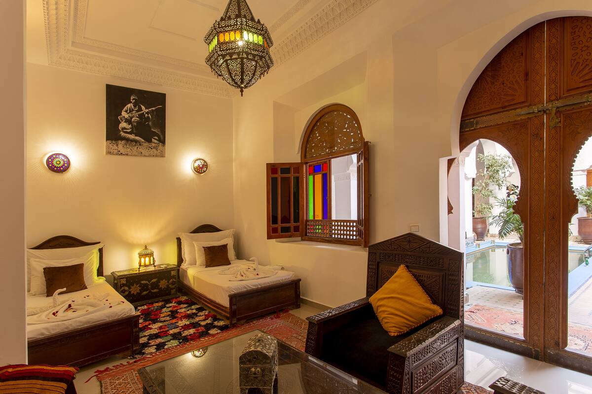 A room with two beds, a sofa, a chandelier, and a view of the outside.