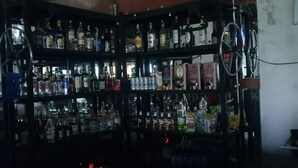 A dimly lit bar with shelves stocked with various bottles and boxes of alcohol. - Albizia Club Nakuru (Sobea)