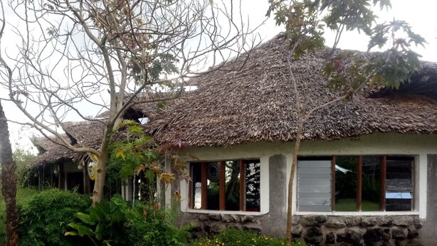 A rustic building with a thatched roof, stone walls, and large windows. - Albizia Club Nakuru (Sobea)