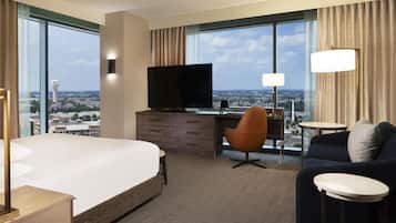 Quarto de hotel com uma cama grande, uma escrivaninha com TV, um sofá e vista para a cidade.