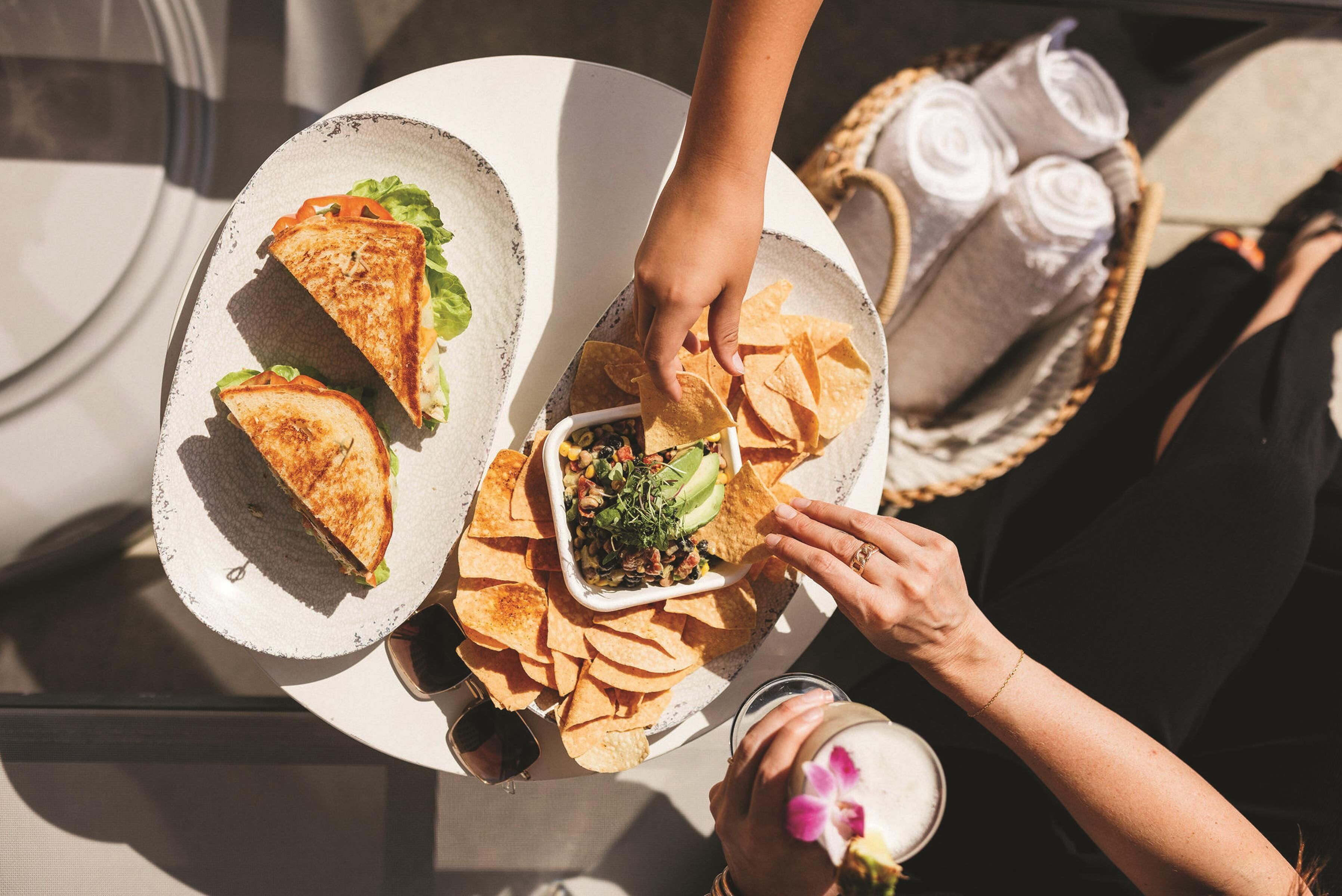 A dining table with a plate of food, a glass of drink, and a basket of rolled towels.