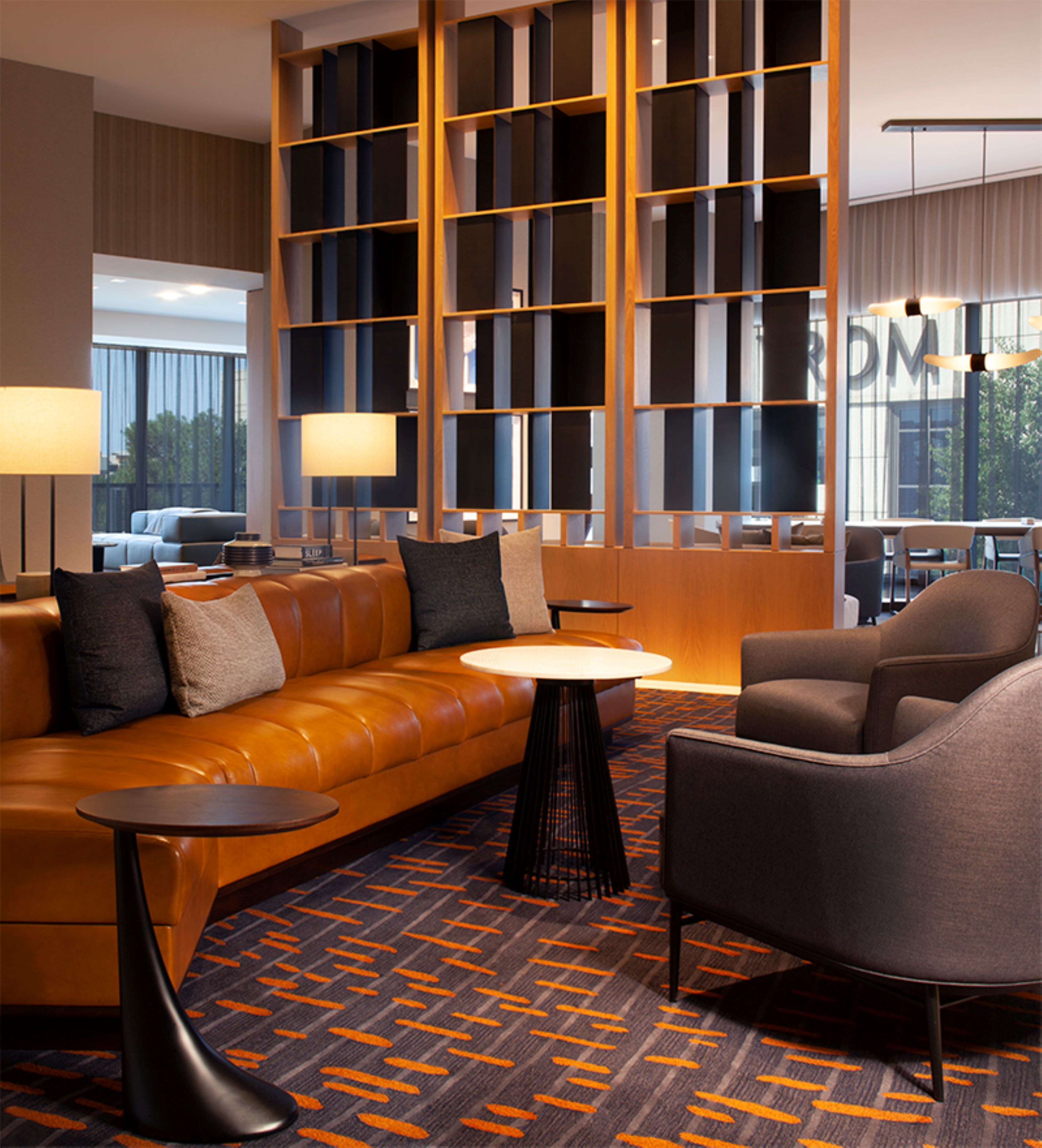 A modern hotel lobby with a leather sofa, armchairs, a small round table, and a patterned carpet.