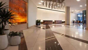 Un hall d’entrée spacieux, doté d’un comptoir d’accueil moderne, de plantes en pot et d’un grand mur orné d’un motif abstrait aux tons chauds.