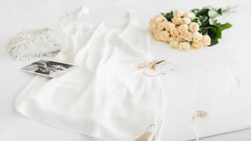A bed with white bedding, a bouquet of flowers, a glass of champagne, and a pair of white shoes.