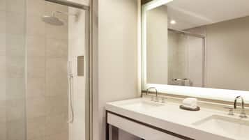 Un baño moderno con ducha de vidrio, un espejo grande y dos lavamanos.