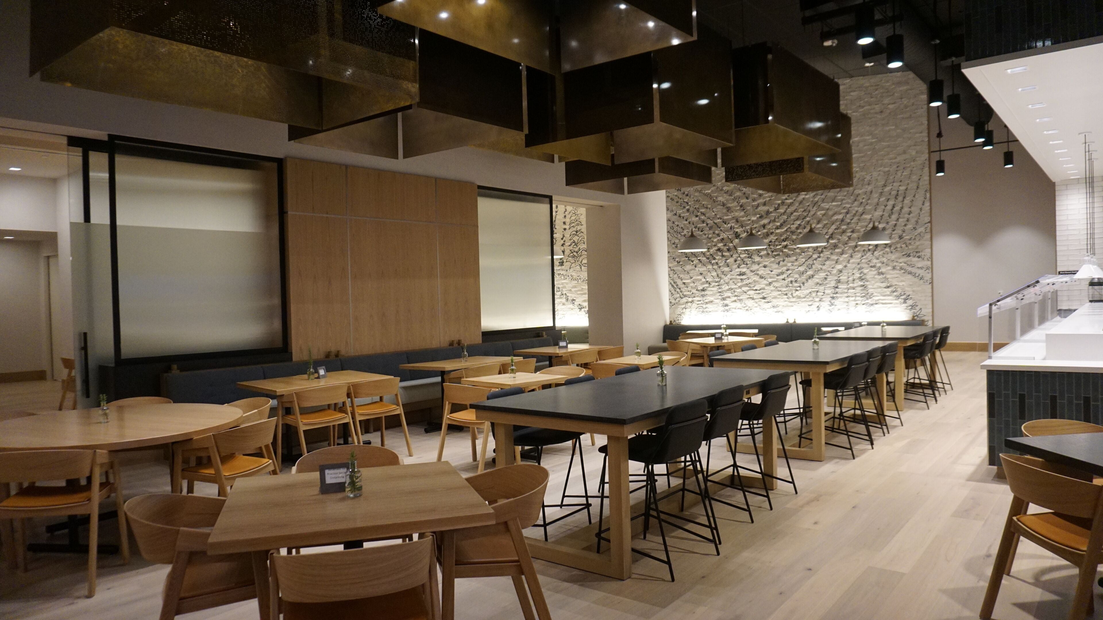 A modern dining area with multiple tables and chairs, a bar area, and a patterned wall.