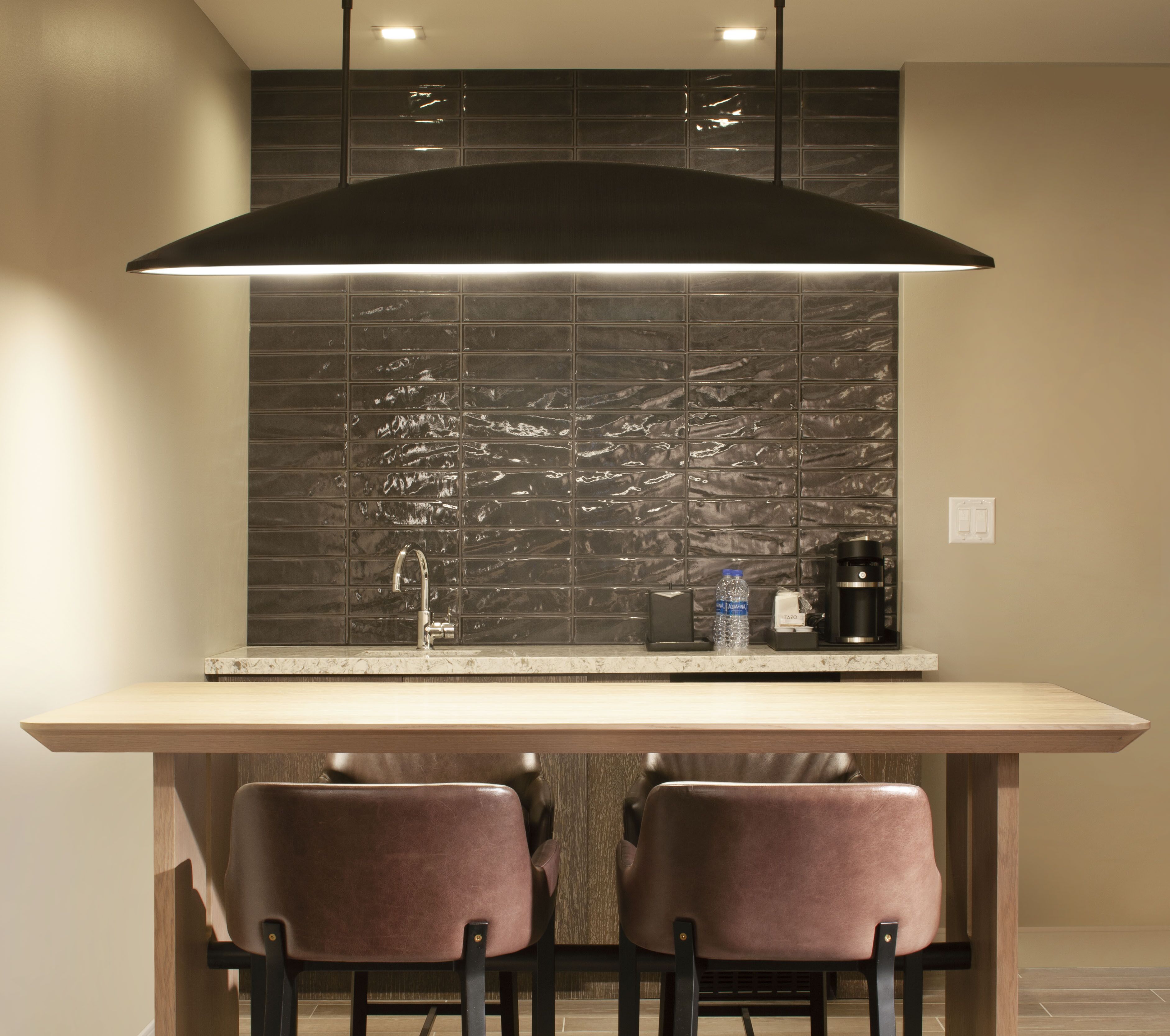 A modern kitchen with a dark backsplash, a stainless steel range hood, and two bar stools.