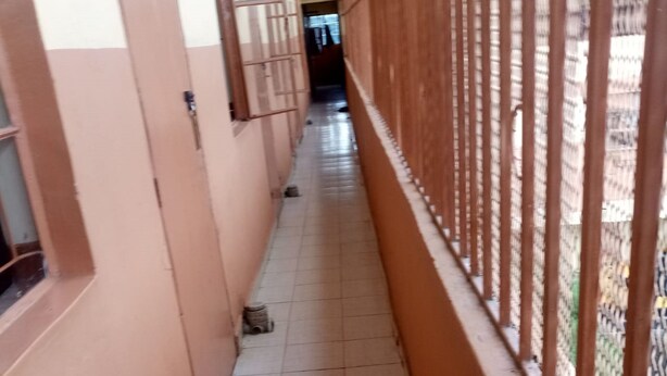 A corridor with tiled flooring, a metal gate on the right, and a window on the left. - Amigos Guest House (Nakuru)