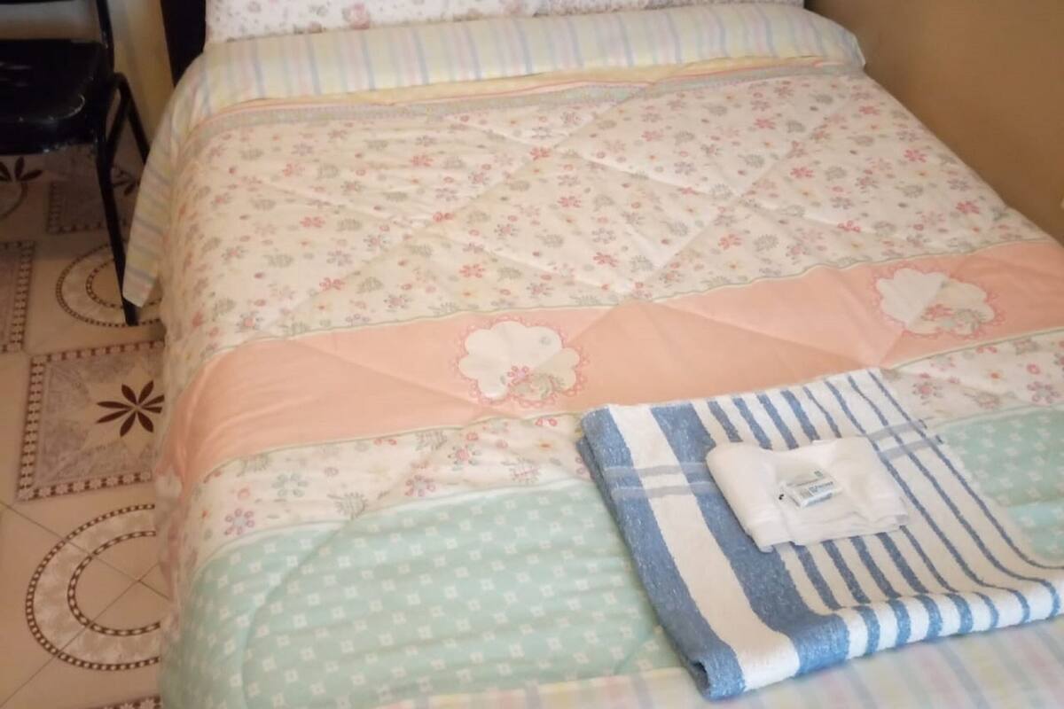 A bed with floral bedding, a quilt, and a folded towel.