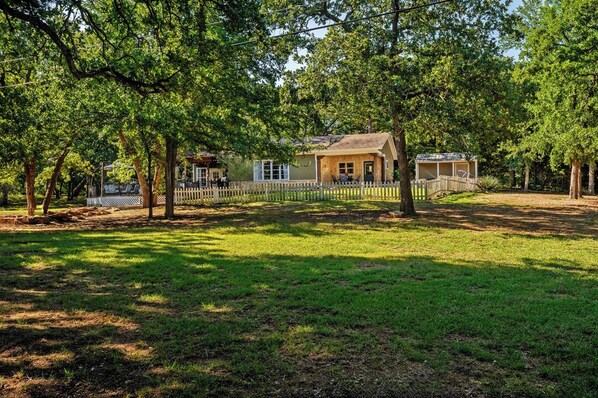 A rustic cabin with a wooden deck, surrounded by lush green trees and a fenced yard. - Texoma/Tanglewood Highport Marina - Adorable Cottage!
(Pottsboro)