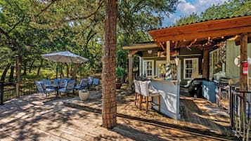Une terrasse en bois avec des sièges extérieurs, un coin bar et une pergola illuminée de guirlandes lumineuses.