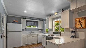 A kitchen with white cabinetry, a built-in oven, a refrigerator, and a window with a view of greenery.