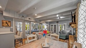 A spacious living area with a wooden dining table, a vase with flowers, and a large window providing a view of the outdoors.