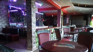 A restaurant with red chairs and tables, a bar area with neon lights, and a stone pillar. - Bahamas Resort (Thika)