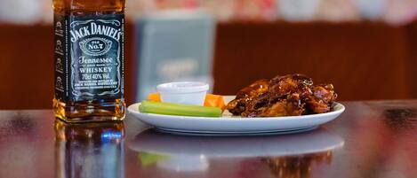 A bottle of Jack Daniel's Tennessee Whiskey and a plate with chicken wings, celery, and a small bowl of sauce on a table.