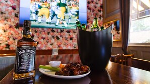 Una botella de whisky Jack Daniel's, un plato con costillas, apio y salsa, y un cubo con botellas de cerveza sobre una barra.