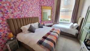 Habitación de hotel con dos camas, un espejo grande, una ventana con cortinas y un papel tapiz floral.