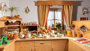 A cozy breakfast setup with a wooden counter, various breakfast items, and a window with curtains. - Ferienwohnung Watzmannblick 55 qm, 1 sep. Schlafzimmer 2-3 Pers. (Berchtesgaden)