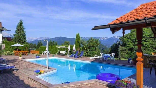 A swimming pool with lounge chairs and umbrellas, surrounded by greenery and mountains in the background. - Ferienwohnung Watzmannblick 55 qm, 1 sep. Schlafzimmer 2-3 Pers. (Berchtesgaden)