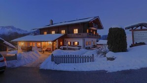 A two-story chalet with a snow-covered driveway and a wooden fence. - Ferienwohnung Watzmannblick 55 qm, 1 sep. Schlafzimmer 2-3 Pers. (Berchtesgaden)