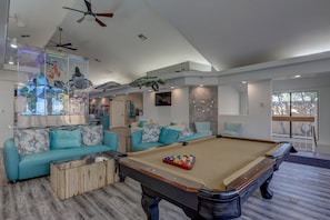 Un salon moderne avec une table de billard, des canapés turquoise et des ventilateurs de plafond.