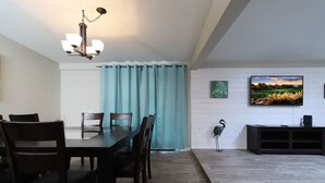 A dining area with a table and chairs, a television mounted on the wall, and a decorative plant. - Spacious Remodel-Great Freeway access-Sleeps 12 (Tucson)