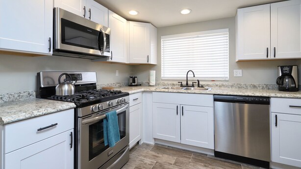 A modern kitchen with white cabinets, stainless steel appliances, a granite countertop, and a window with blinds. - Spacious Remodel-Great Freeway access-Sleeps 12 (Tucson)