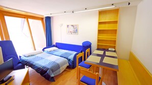 Una habitación pequeña con cama, escritorio, silla y una mesita.