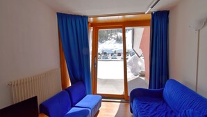 Una habitación con dos sofás azules, una mesa de madera y un amplio ventanal que da a un paisaje nevado.