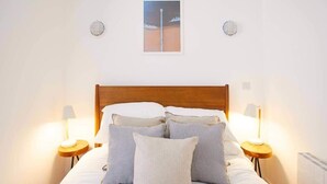 Una cama bien hecha con almohadas y dos lámparas de noche, un cuadro enmarcado en la pared y un cabecero de madera.