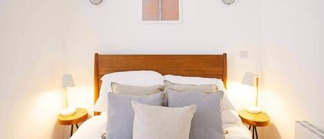 Una cama bien hecha con almohadas y dos lámparas de noche, un cuadro enmarcado en la pared y un cabecero de madera.