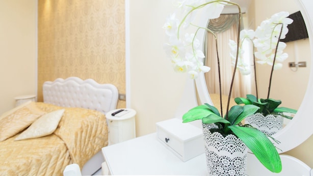 Une chambre à coucher avec un lit, une table de chevet, un miroir et un vase de fleurs.