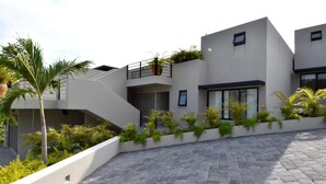 A modern building with a flat roof, a balcony with a metal railing, and a paved courtyard. - Agaves 203 (Santa María Huatulco)
